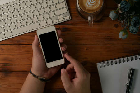 Above view and table top view with male hands using smartphone on the wooden table with modern keyboard, latte coffee and writing note.の写真素材