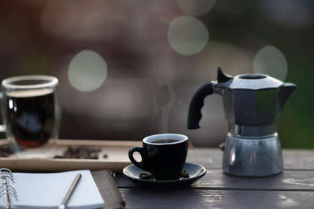 Closed up with a hot coffee, moka pot and note papers place on the wooden table with bokeh background.の写真素材