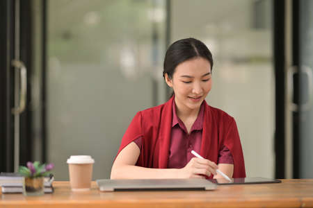 An attractive Asian businesswoman sitting in front of laptop and managing small business from her office.の写真素材