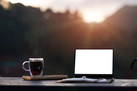 The view of the mountain when the sun rises with a tablet, cup of black coffee and note on the wooden table.の写真素材