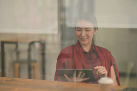 Portrait and though the window view with Asian woman who smile because of her tablet,の写真素材