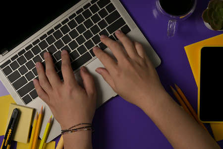 Top view with purple background and human hands typing on laptopの写真素材