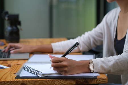 Closed up with woman sitting at office desk while taking note, the other hand typing computer.の写真素材