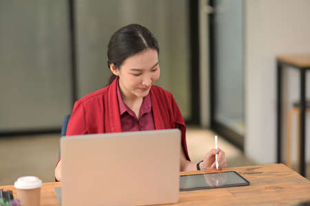 Portrait with Asian businesswoman using stylus pen writing on tablet in front of laptop computer, Working woman concept.の写真素材