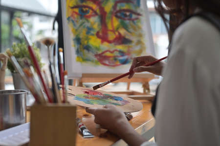 Cropped image of young beautiful artist girl mixing an oil color at the modern studio. Art,...
