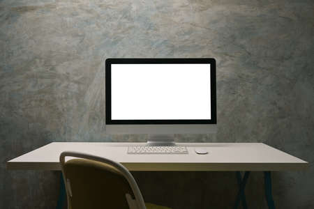 White blank screen computer monitor putting on the modern desk over cement wall as a background.