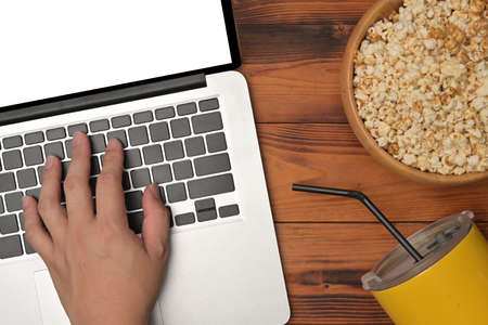 Top view of hand using a white screen computer laptop at the wooden table surrounded by popcorn bowl...