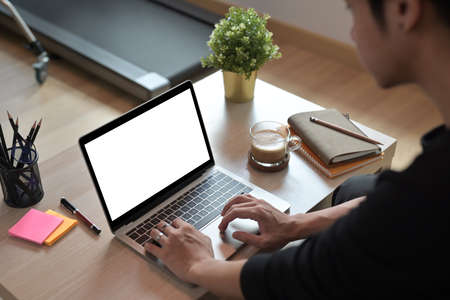 Closed up of a young man working with a white blank screen laptop at the comfortable working desk.