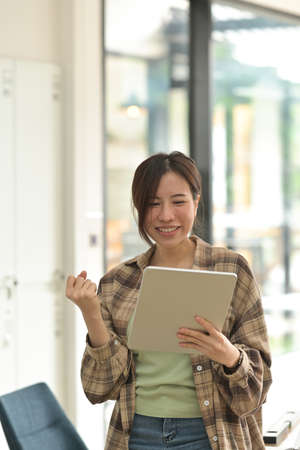 Photo of an attractive woman celebrate pose and holding a digital tablet and celebrating goal achievement.の写真素材