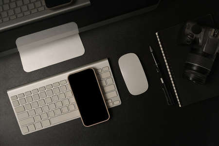 Tabletop view with a computer monitor, blank screen smartphone, digital camera, notebook, pen, wireless mouse and keyboard on the black backgroundの写真素材