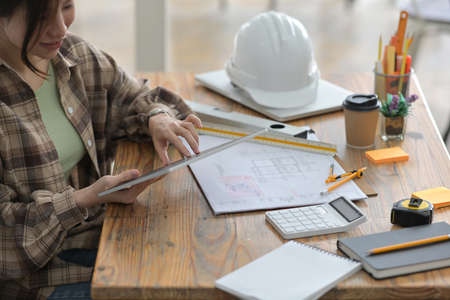Cropped image of an architect woman's hands is holding a digital tablet at the wooden working desk.の写真素材