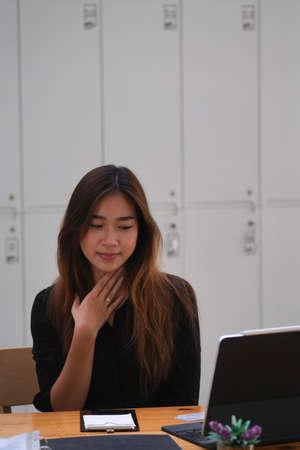 Portrait of young woman touching neck and looking at the digital tablet that putting on a wooden...