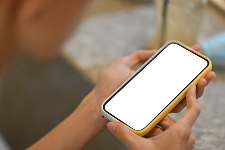 Close-up image of woman's hand holding a white blank screen smartphone in the comfortable living room.の写真素材
