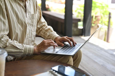 Cropped image of a young man typing on a computer laptop that putting on his lap while sitting at...