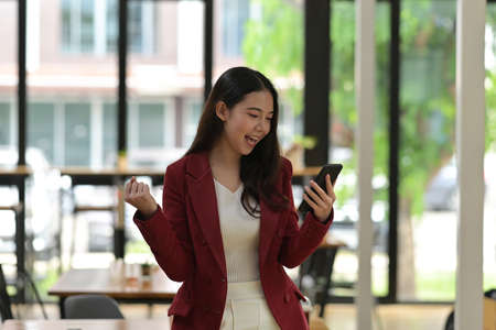 Photo of a businesswoman makes a winner gesture and holding a smartphone in the modern office.の写真素材