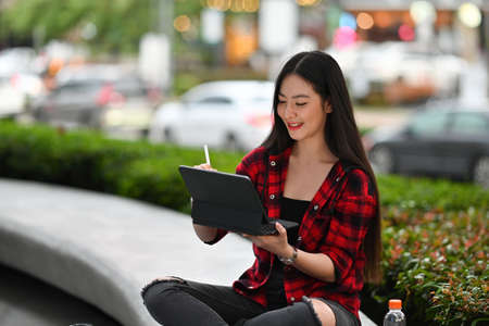 Photo of a beautiful woman using a digital tablet and stylus pen while sitting and relaxing at the...