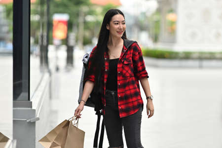 Photo of a fashionable woman carrying shopping paper bags in front of the shopping mall as a...