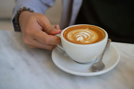 Closeup image of a young smart man holding a coffee cup with latte art in the comfortable living...
