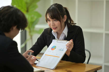 Photo of beautiful businesswoman teaching her new colleague about work at the wooden table.