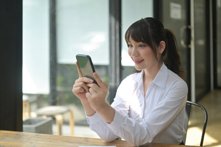 Photo of a beautiful woman using a smartphone while sitting at the wooden working in the comfortable...