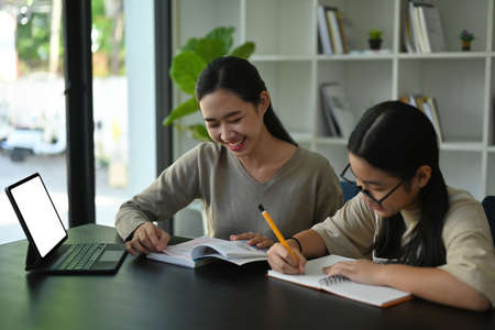 Photo of a young mother doing homework together with her daughter at the wooden student desk.の写真素材