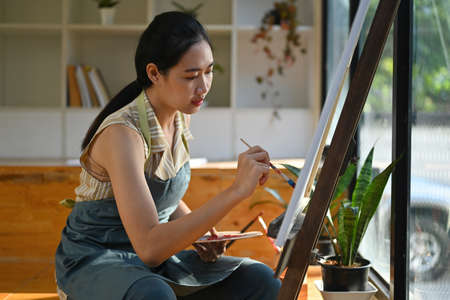 Portrait of the young talented female artist making sketches in the comfortable art studio.