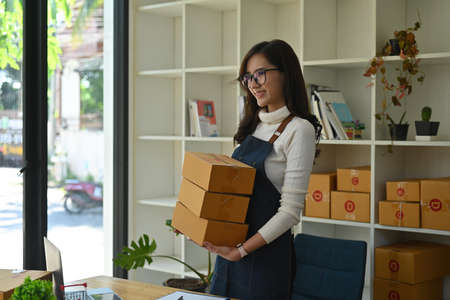 Photo of a young business owner standing and holding cardboard boxes in the comfortable living room...