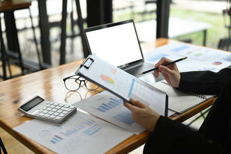 Close-up image of an insurance agent holding a clipboard at the wooden working desk surrounded by a white blank screen computer laptop and office equipment.の写真素材