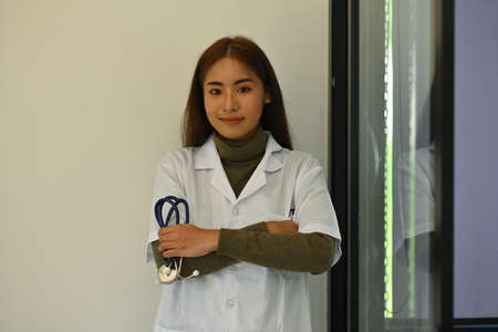 Photo of a young female doctor standing with arm crossed and holding a stethoscope in hand over the...