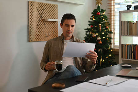Photo of a young man looking on paperwork and relaxing with a coffee at the comfortable working desk.の写真素材