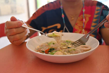 Close-up image of a woman while eating Stir-fried noodles with savory sauce at the lunch table.