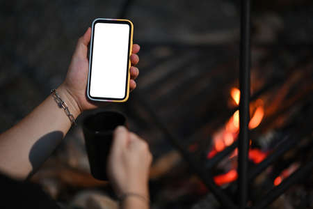 Behind view of a tourist hand holding a white blank screen smartphone and coffee cup over the as...