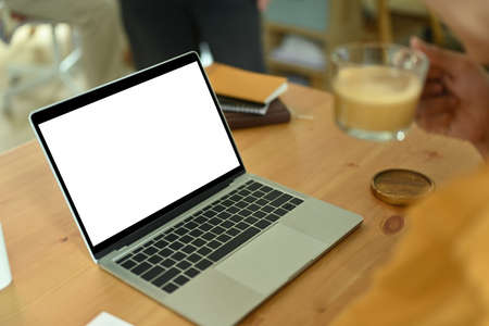 Close-up image of a freelance man holding a coffee cup at the wooden working desk surrounded with a white blank screen computer laptop and personal equipment.の写真素材