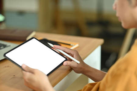 Photo of a young smart man using a white blank screen digital tablet and stylus pen for on site...