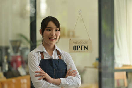 Photo of a young coffee shop owner standing with crossed arms in front of the glass door.の写真素材