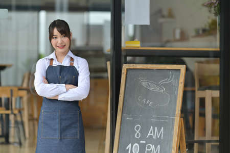 Photo of a young coffee shop owner wearing an apron and standing over the coffee shop signboard.の写真素材