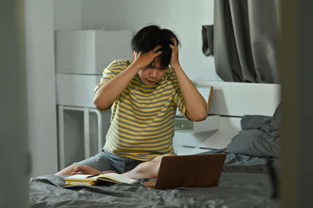 Photo of a stressed man keeps a hand on the head while tutoring a lesson from the university on the...