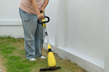 Cropped image of a gardener cutting grass by a lawnmower.