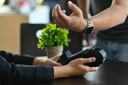 Photo of a young man using a smartwatch for doing a payment at the automatic payment machine.