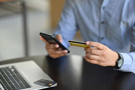 Cropped image of a young businessman holding a credit card and smartphone for doing an online...