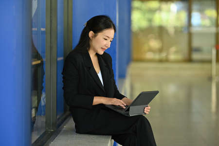 Portrait with Asian businesswoman in black suit using tablet while sitting  on bench.の写真素材