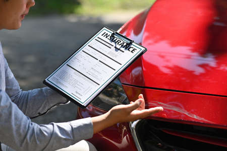 Photo of an insurance agent with clipboard checking damage after a car crash.