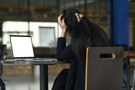 Photo of a stressed businesswoman sitting at the office desk surrounded by a computer laptop and digital tablet.の写真素材