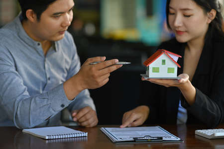 Photo of a young man talking with a businesswoman while holding a house model at a comfortable...