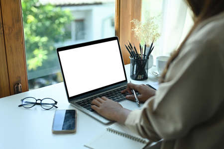Cropped image of a businesswoman typing on a white blank screen computer laptop at the modern office...