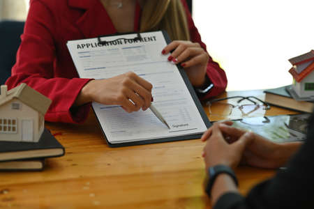 Photo of a real estate agent suggesting her customer sign a document on the clipboard.の写真素材