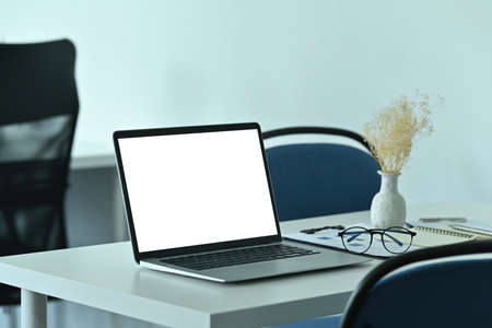 Photo of a comfortable workspace surrounded by a white blank screen computer laptop and various...