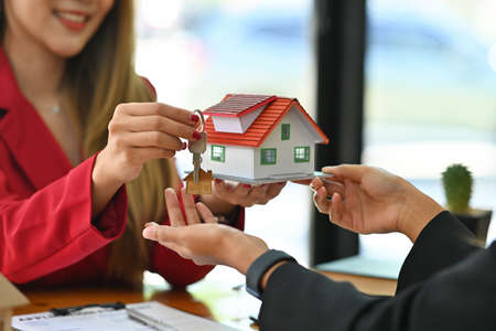 Photo of a young broker woman showing a house model while sitting together with her customer at the wooden working desk.の写真素材
