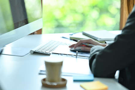 Cropped image of a young office woman working with a computer at the modern office desk surrounded...