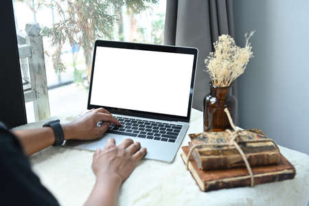 Photo of a man using a white blank screen computer laptop at the table surrounded by a stack of old...